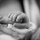 grayscale photography of baby holding finger